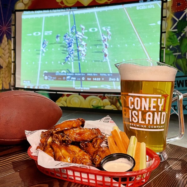 THE BIG GAME - FOOTBALL ON PROJECTOR SCREEN WITH WINGS, A FOOTBALL AND A PITCHER OF BEER ON A TABLE