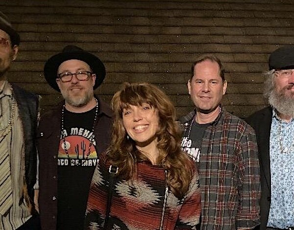 Image of band members standing in front of a brick wall.